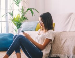 Serious woman in eyeglasses text messaging using mobile phone while sitting on floor