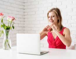 Valentines Day. Beautiful woman in pink dress dating online making heart with her hands
