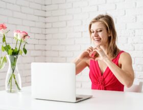 Valentines Day. Beautiful woman in pink dress dating online making heart with her hands