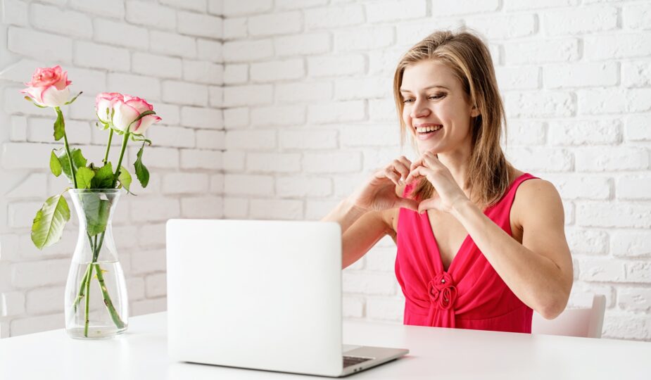 Valentines Day. Beautiful woman in pink dress dating online making heart with her hands