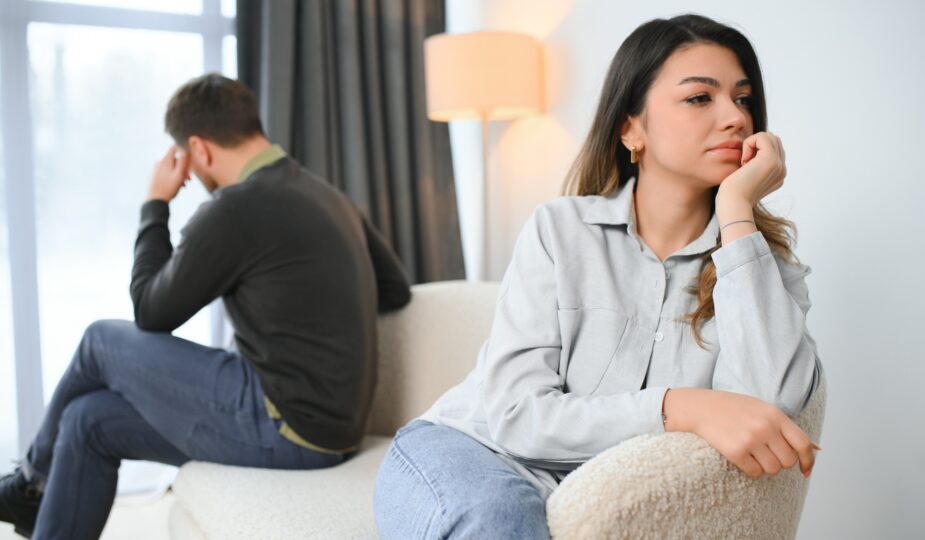 Beautiful couple is sitting back to back on the couch while having a quarrel