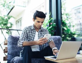 Caucaisan male blogger checking received email while sending sms message on mobile phone