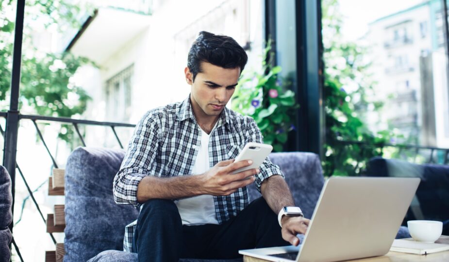 Caucaisan male blogger checking received email while sending sms message on mobile phone