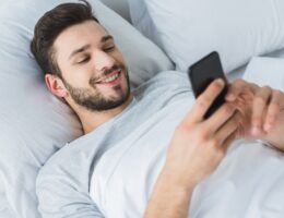 happy bearded man using smartphone in bed in the morning