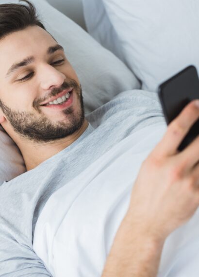 happy bearded man using smartphone in bed in the morning