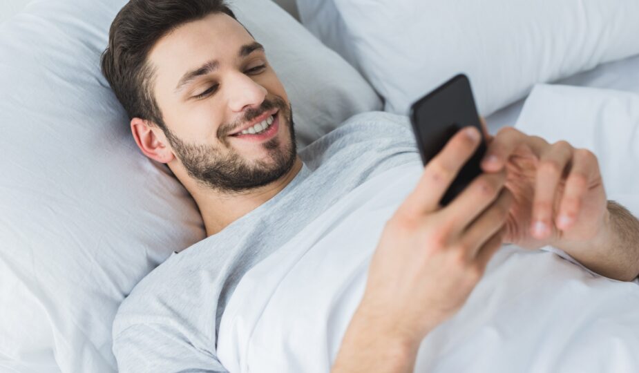 happy bearded man using smartphone in bed in the morning