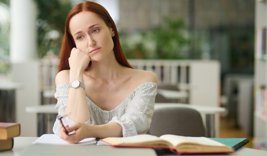 Sad woman sitting at table with books