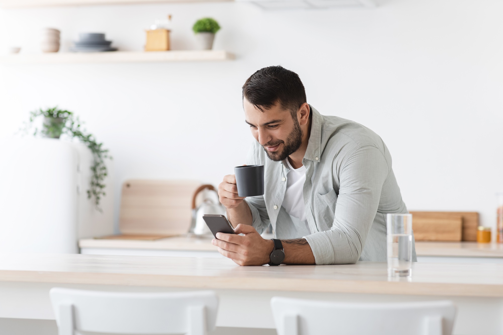 Smiling handsome mature european guy drinking coffee and reading news on smartphone, chatting