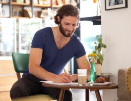 Smiling young man sitting in a coffee shop writing letter