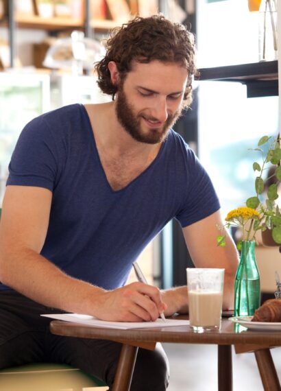 Smiling young man sitting in a coffee shop writing letter
