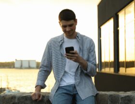 Young man uses a phone outdoor. Writing a message