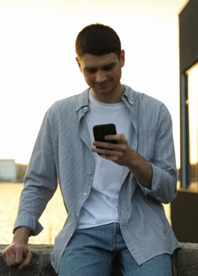 Young man uses a phone outdoor. Writing a message