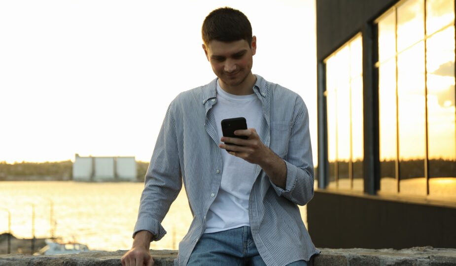 Young man uses a phone outdoor. Writing a message